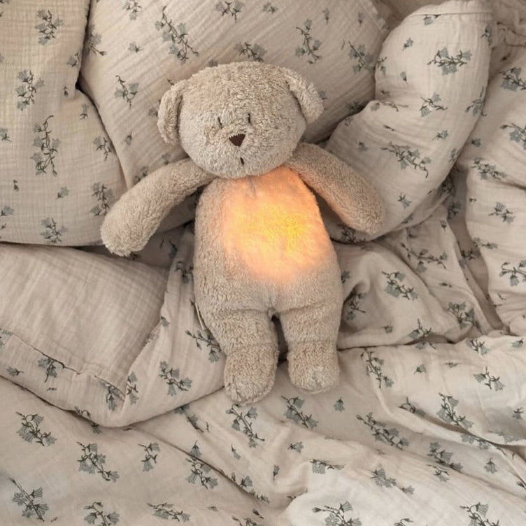 Fluffy Moonie teddy bear with a glowing light on a floral-patterned blanket