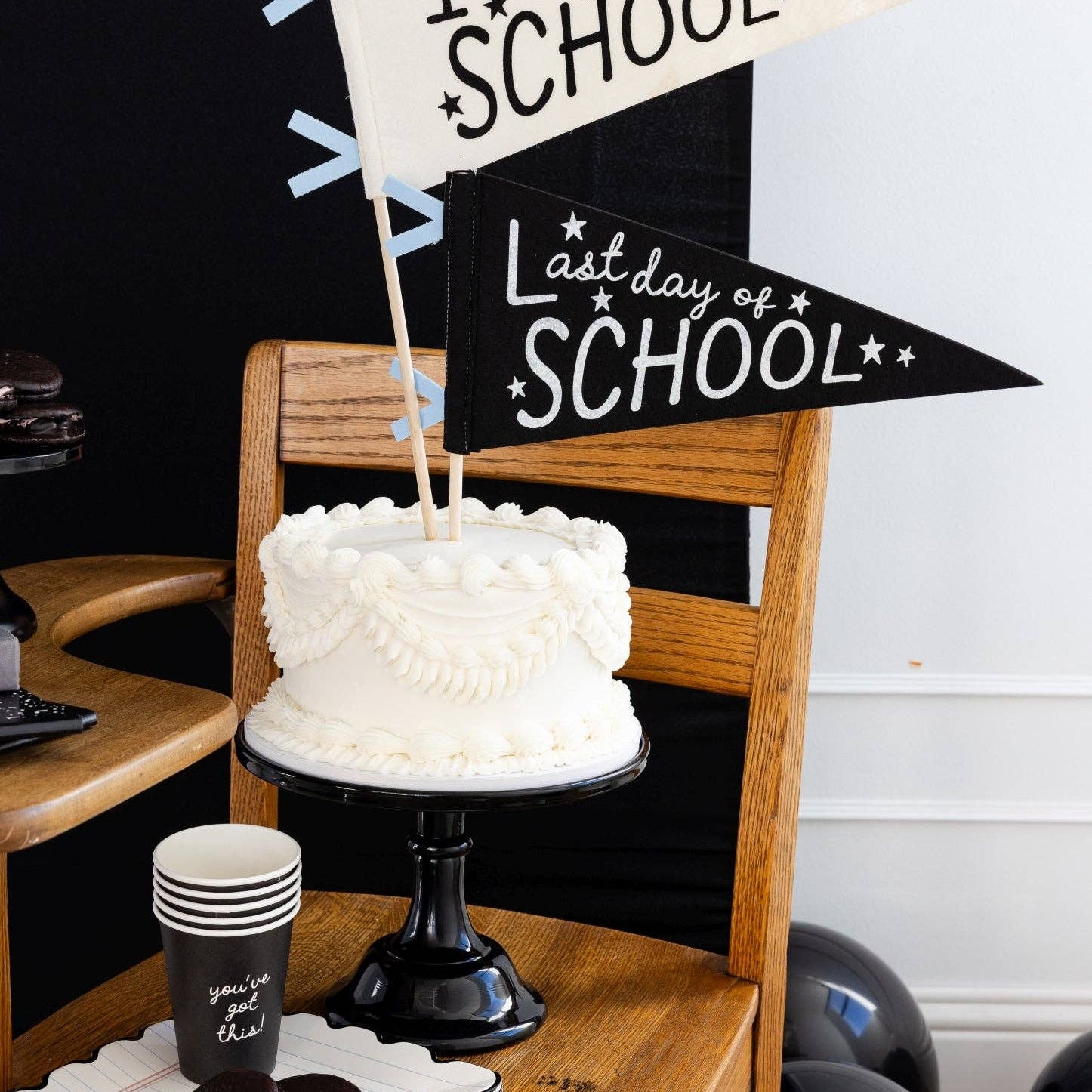 White cake on a wooden stand with '1st Day of School' and 'Last Day of School' signs.