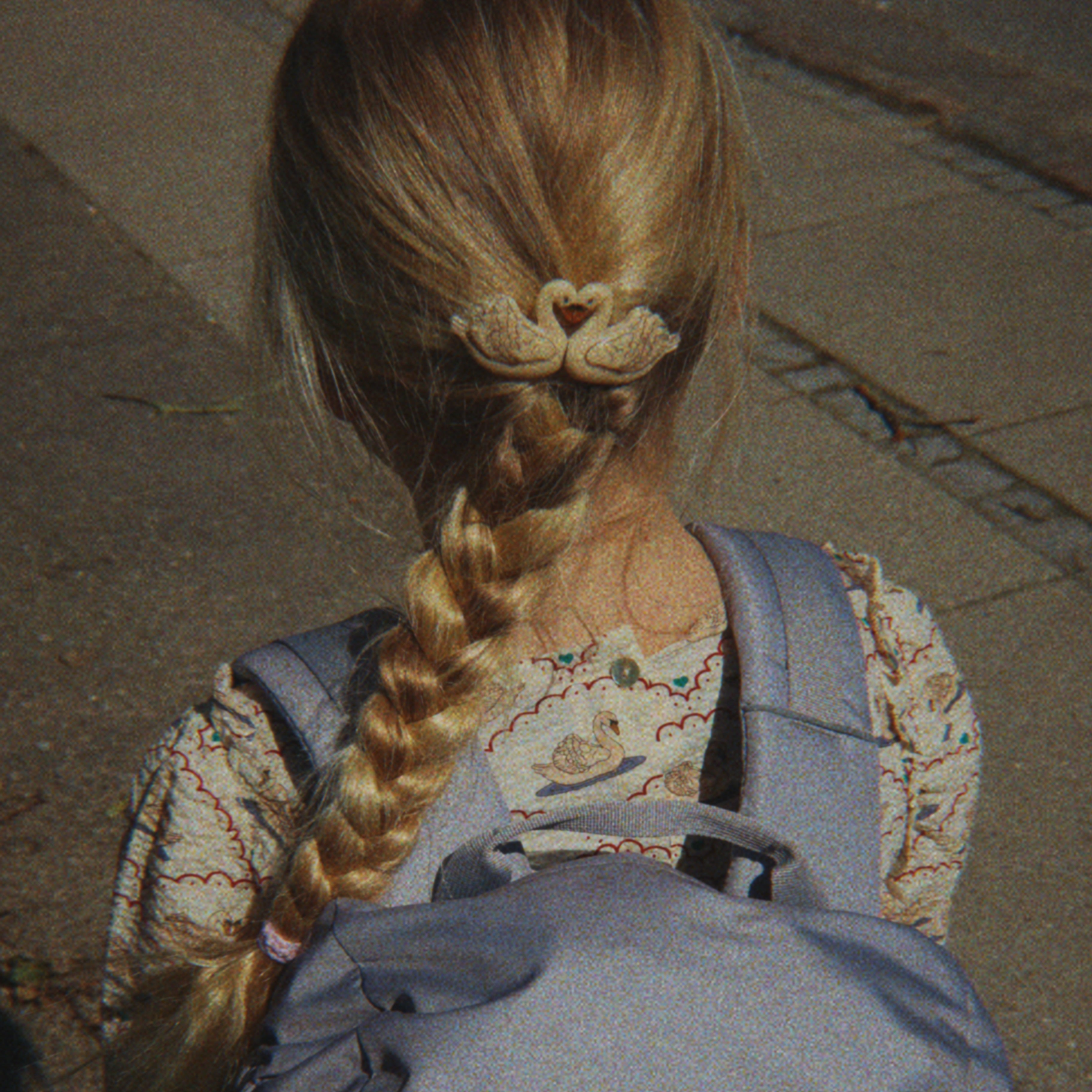 Person with braided hair wearing a gray backpack with swan designs.