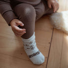 A close-up of a child wearing ribbed brown leggings and white socks with dark brown paw prints and the word 'aming' printed on the sole, sitting on a light wood floor.