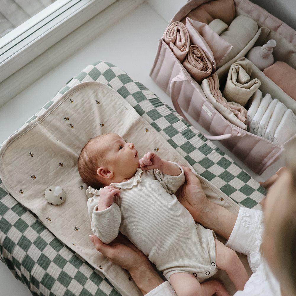 Newborn baby lying on a checkered blanket with a folded outfit set in the background.