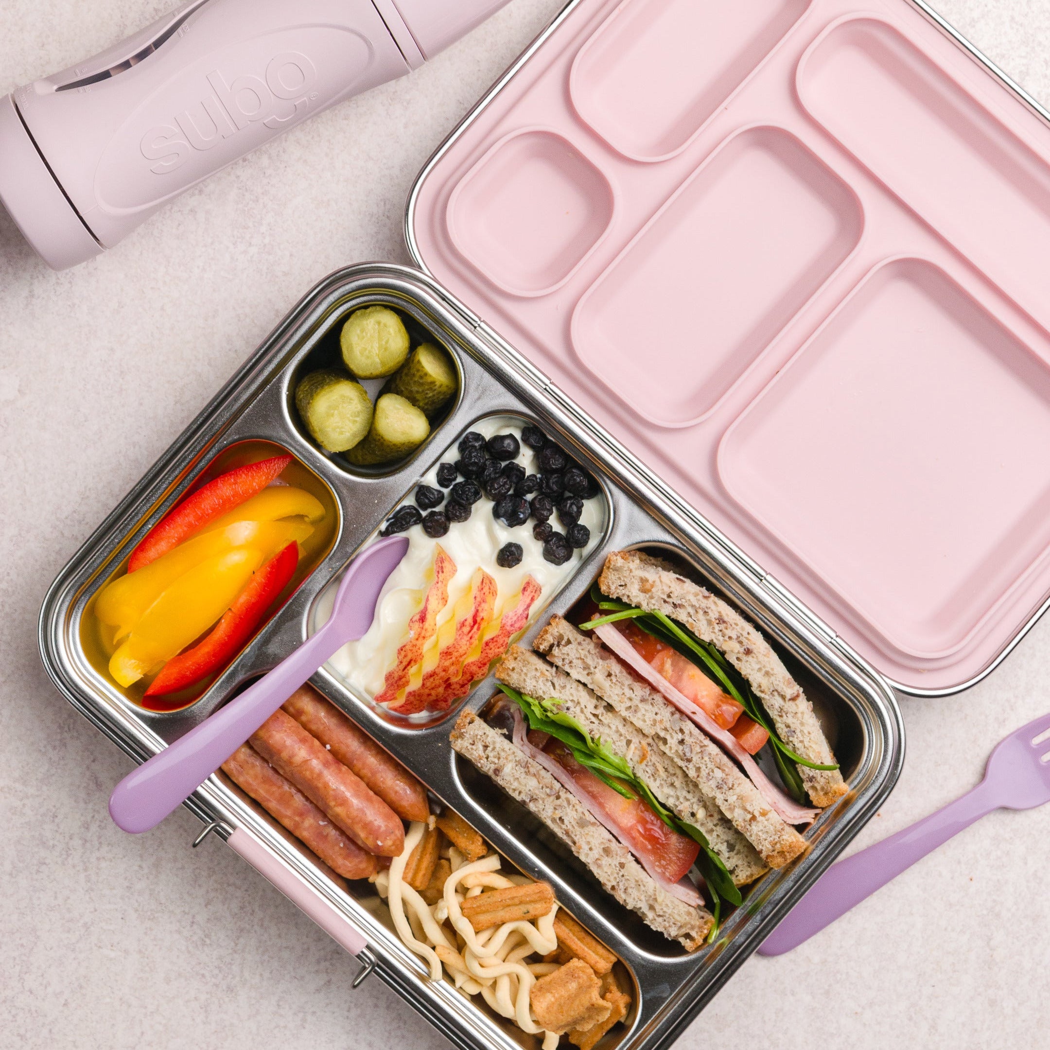 Pink bento box with compartments containing a variety of food items on a light gray background.