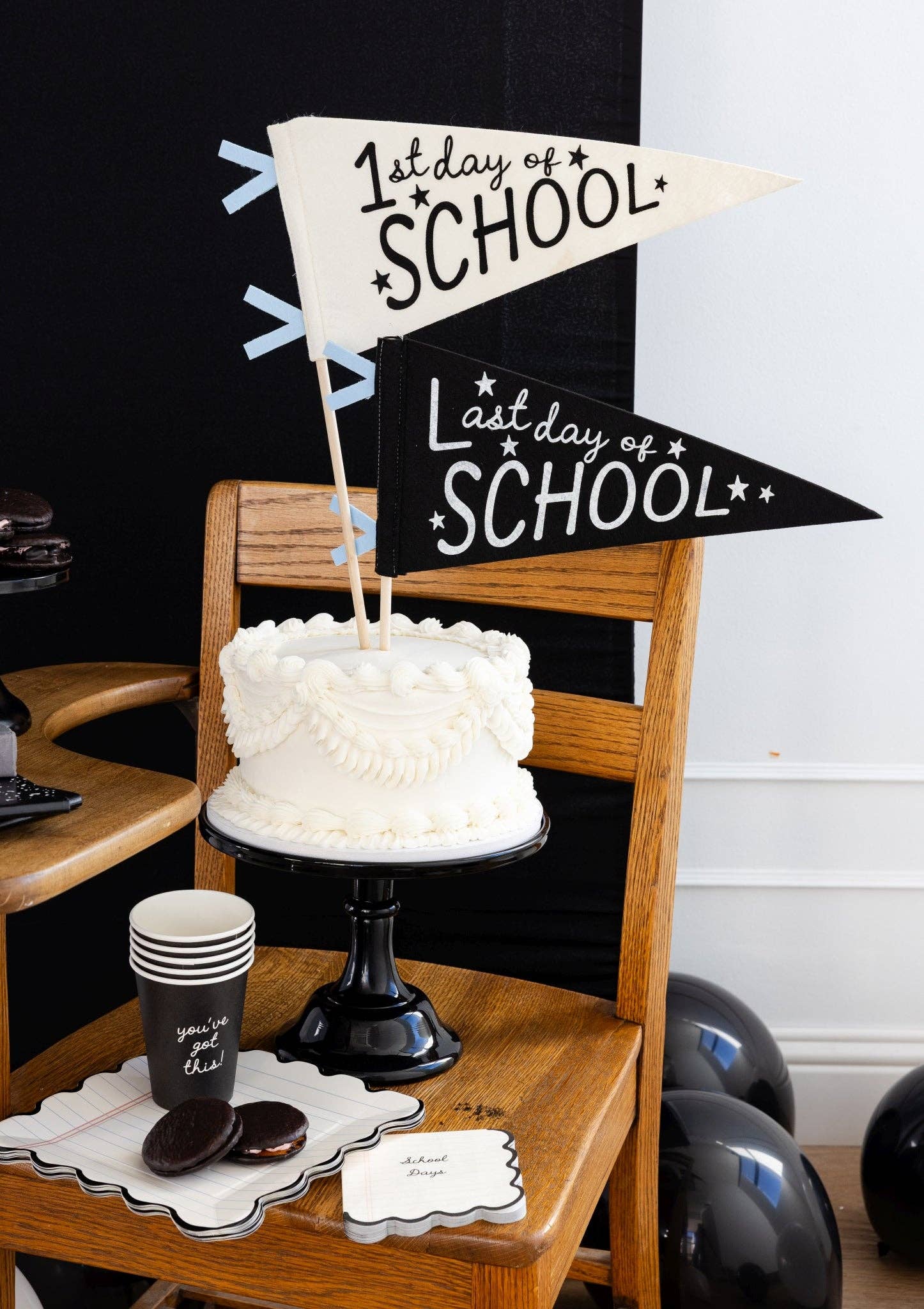 White cake on a wooden stand with '1st Day of School' and 'Last Day of School' signs.