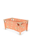 A wooden doll bed with peach fabric sides and back panels featuring a small cat print, shown on a plain white background.