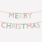 Merry Christmas letter banner with glittery letters on a red string, displayed against a plain light gray background.