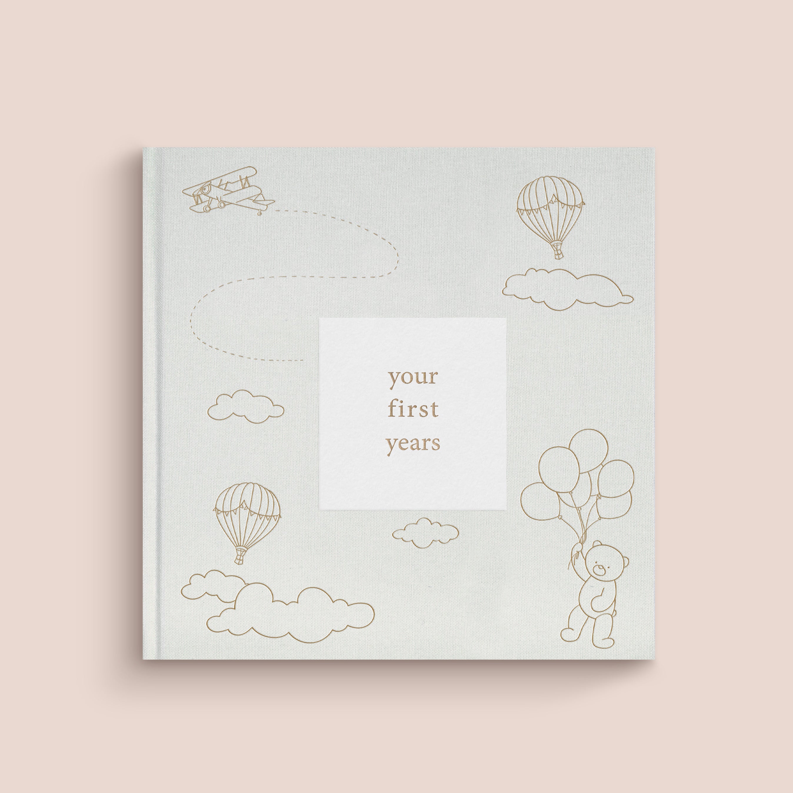 A beige baby record book with gold foil details and illustrations of a baby, balloons, and clouds on the cover. The title 'your first years' is displayed.